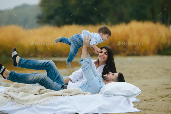 Happy young family relaxing together on the lake Stock Photo by simbiothy