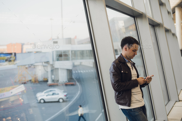Young business man in airport using smartphone . Stock Photo by romankosolapov