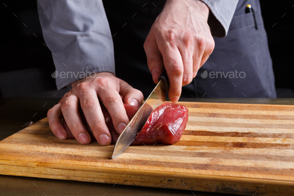 Chef cutting filet mignon on wooden board at restaurant kitchen Stock Photo by Milkosx