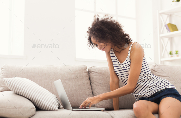 Young girl with laptop sitting on beige couch Stock Photo by Milkosx