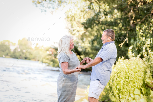 Elderly couple holding hands by the lake. Stock Photo by photocreo