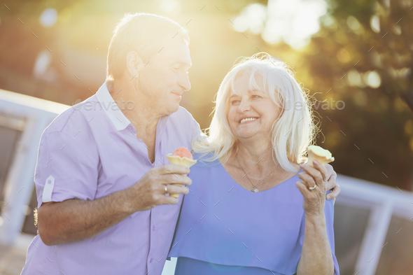 Older couple eating ice cream and walking. Stock Photo by photocreo