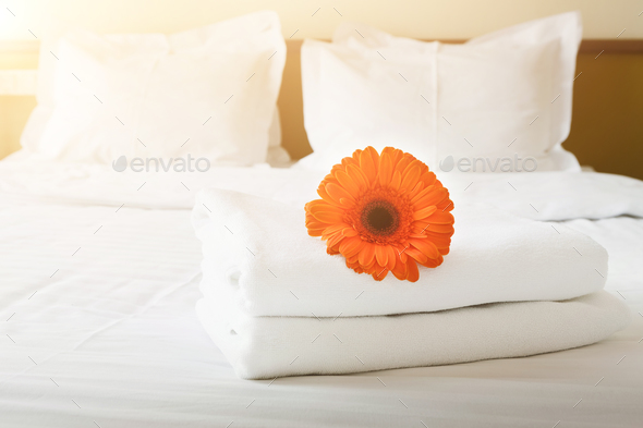 Stack of towels and flower on bed in hotel room Stock Photo by Milkosx
