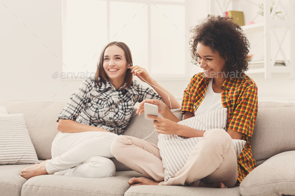 Two women listening music and sharing earphones Stock Photo by Milkosx