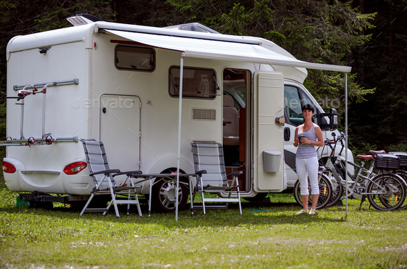 Woman is standing with a mug of coffee near the camper RV. Stock Photo by cookelma