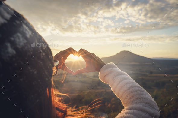 Young woman traveler making heart shape symbol at sunrise Stock Photo by kitzstocker