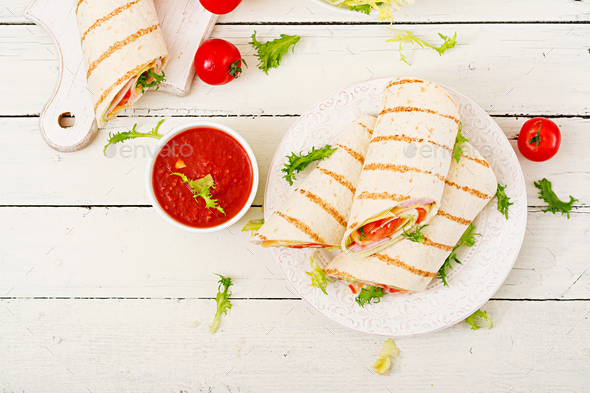 Tortilla wrap with ham, cheese and tomatoes on a white wooden background. Top view Stock Photo by Timolina