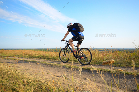 Male cyclist with backpack driving by rural dirt road outdoors Stock Photo by e_mikh