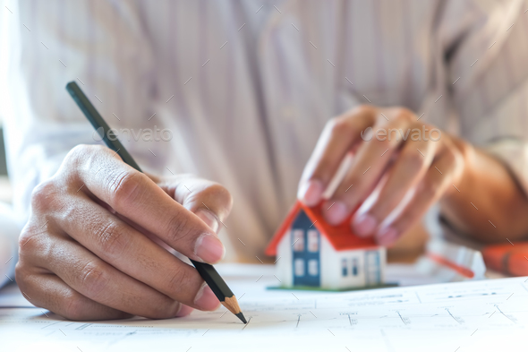 Architects are writing home,other hand captures the model house. Stock Photo by sarawutnirothon