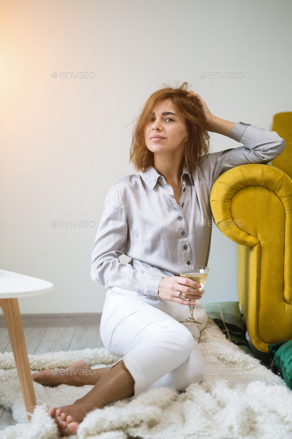 A beautiful young woman siting on a couch with a glass of wine Stock Photo by ollinka