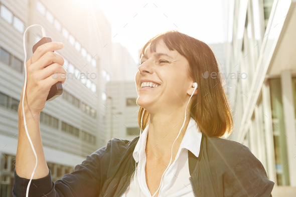 Happy woman holding cellphone with earphones in sunlight Stock Photo by mimagephotography