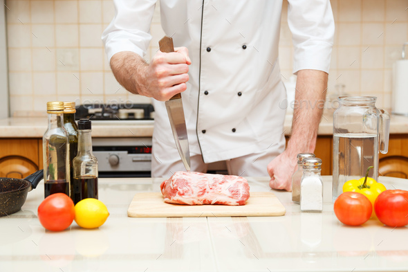 Butcher cutting meat on chopping board, professional cook holding knife and cutting meat. Stock Photo by Vladdeep