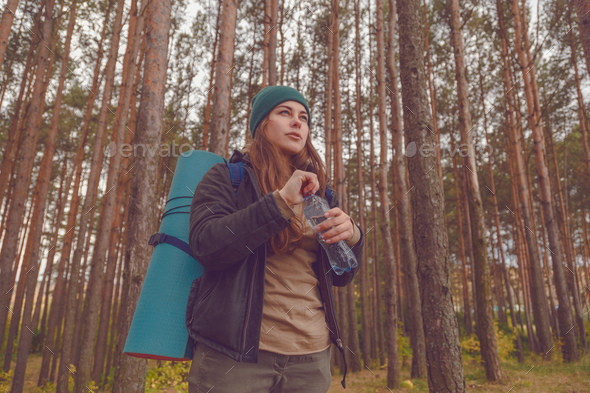 Hiker girl enjoying water. Happy woman tourist with backpack drinking water from bottle in nature. Stock Photo by Vladdeep