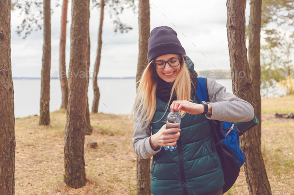 Hiker girl enjoying water. Happy woman tourist with backpack drinking water from bottle in nature. Stock Photo by Vladdeep