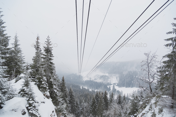 Cableway in the mountains in winter. Perspective view of the mountain woods and rope ropeway Stock Photo by Vladdeep