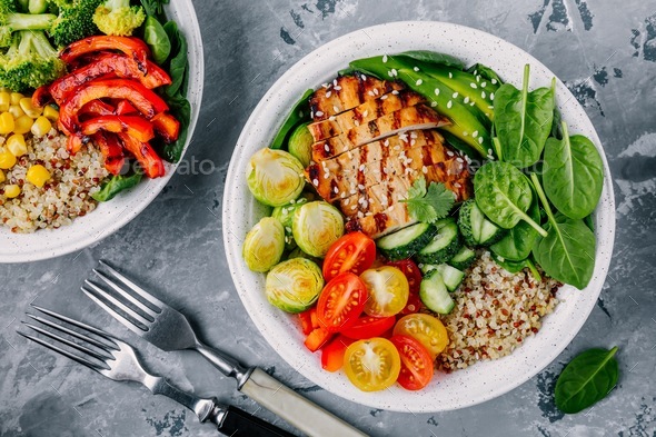 Healthy buddha bowl grilled chicken, quinoa, spinach, avocado, brussels sprouts, tomatoes, cucumbers Stock Photo by nblxer