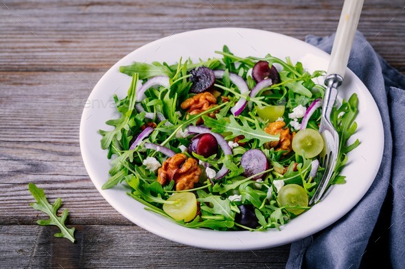 green salad bowl with arugula, walnuts, goat cheese, red onion and grapes Stock Photo by nblxer