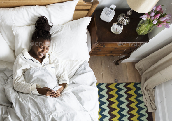 Smiling African American woman on bed using a cellphone Stock Photo by Rawpixel