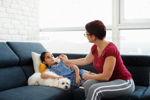 Mother Checking Temperature To Ill Daughter With Thermometer Stock Photo by diego_cervo