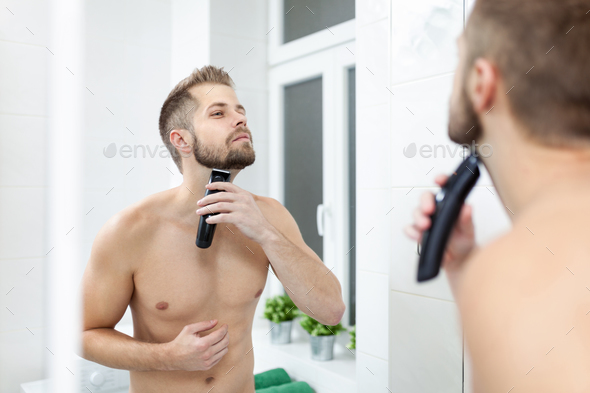 Handsome bearded man trimming his beard with a trimmer Stock Photo by tommyandone