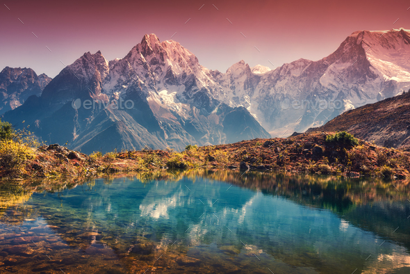Mountains with snow covered peaks, red sky reflected in lake Stock Photo by den-belitsky