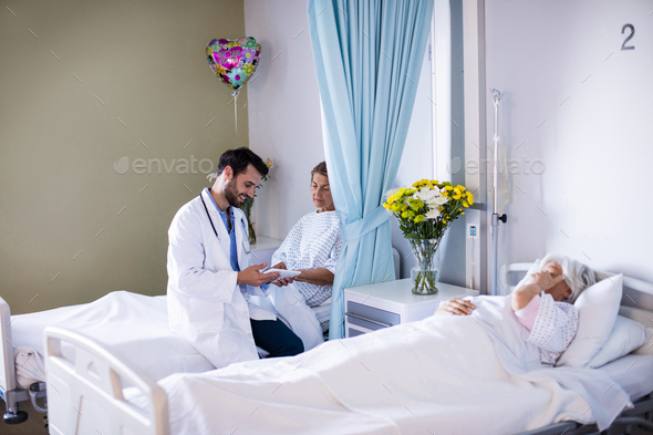 Male doctor interacting with female senior patient in the ward Stock Photo by Wavebreakmedia