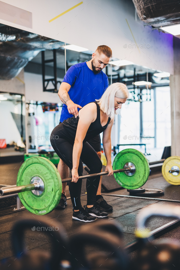 Personal trainer assisting woman lifting weights. Stock Photo by photocreo