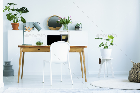 White chair at wooden desk with laptop and lamp in white home of Stock Photo by bialasiewicz