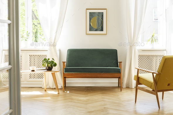 Green sofa with dark, wooden frame and a comfy yellow armchair i Stock Photo by bialasiewicz
