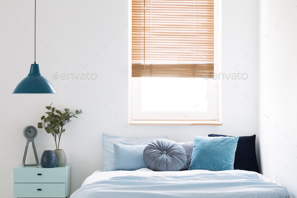 Lamp above blue cabinet with plant next to bed in simple bedroom Stock Photo by bialasiewicz