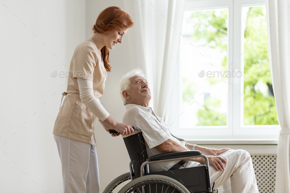 Smiling nurse supporting disabled senior man in the wheelchair Stock Photo by bialasiewicz