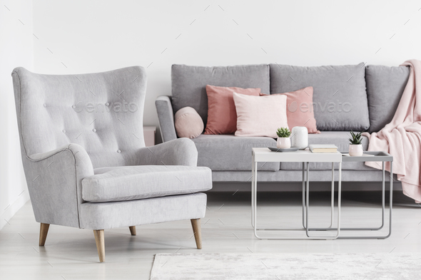 Comfy armchair and grey sofa with pink pillows, and coffee table Stock Photo by bialasiewicz