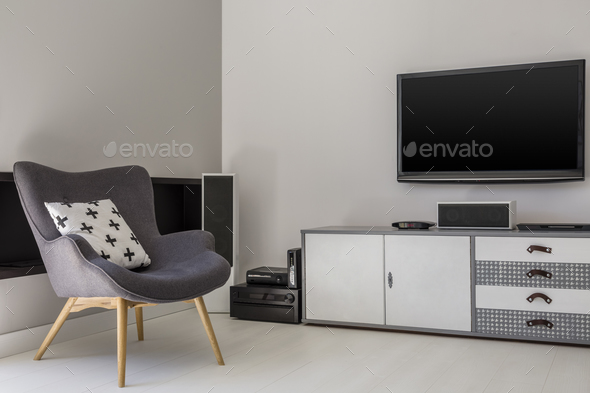 Television above cabinet next to grey armchair with patterned pi Stock Photo by bialasiewicz