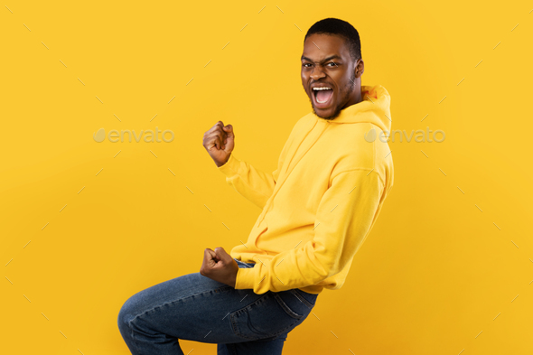 Emotional Black Man Shaking Fists In Joy Over Yellow Background Stock