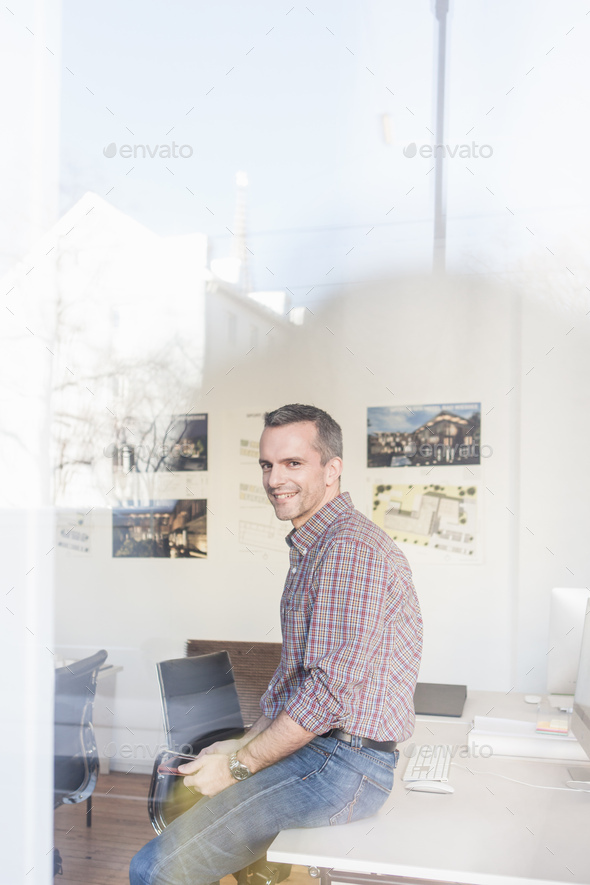 View Through Glass Side View Of Mature Man Sitting On Desk Looking At