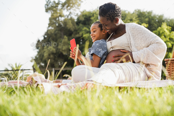 Happy Pregnant Mother And Son Having Fun Using Mobile Phone Outdoor