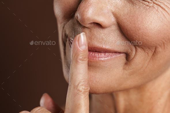 Senior Shirtless Woman Smiling While Showing Silence Gesture Stock