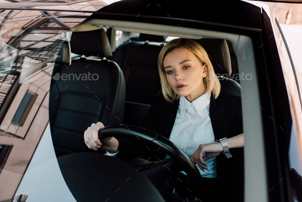 Confident Blonde Woman Holding Steering Wheel While Driving Car Stock