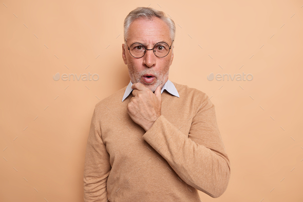 Portrait Of Surprised Mature Man Holds Chin Reacts Emotionally To News