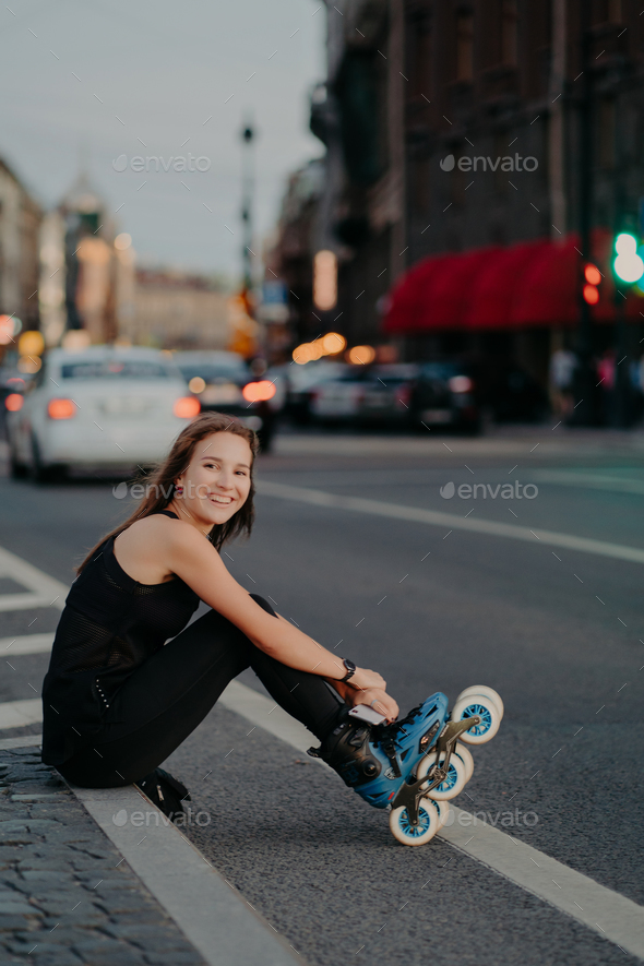 Active Slim Woman Poses On Asphalt Puts On Rollerskates Being In Good