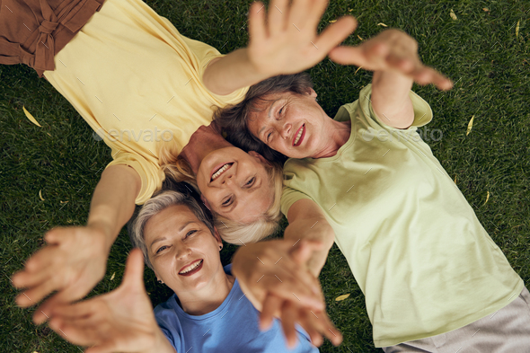 Smiling Mature Women Friends Lying Head To Head On Grass And Extend