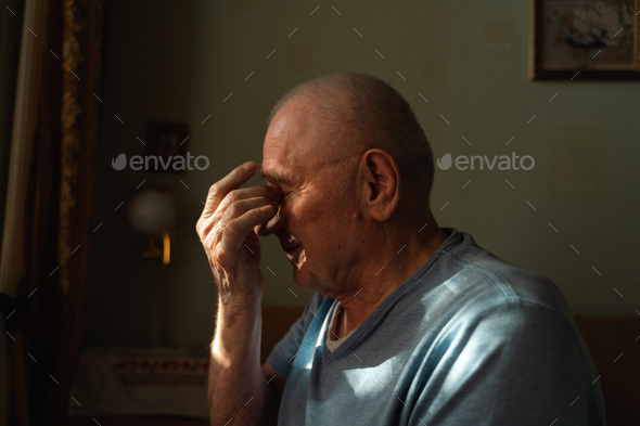 Elderly Senior Man At Home In Shadow And Sunlight With Headache