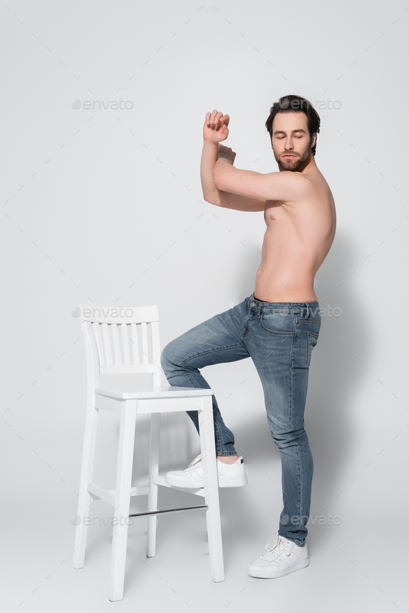 Full Length View Of Shirtless Man In Jeans Posing Near White Chair On Grey Stock Photo By