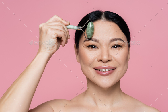 Smiling Asian Woman With Naked Shoulders Massaging Forehead With Jade