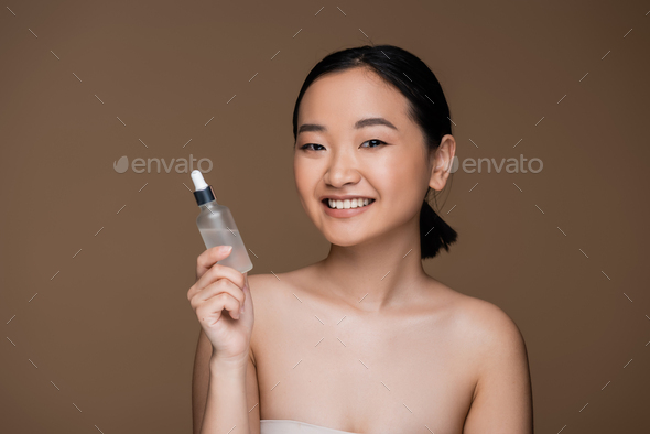 Positive Asian Woman With Naked Shoulders Holding Bottle Of Essential