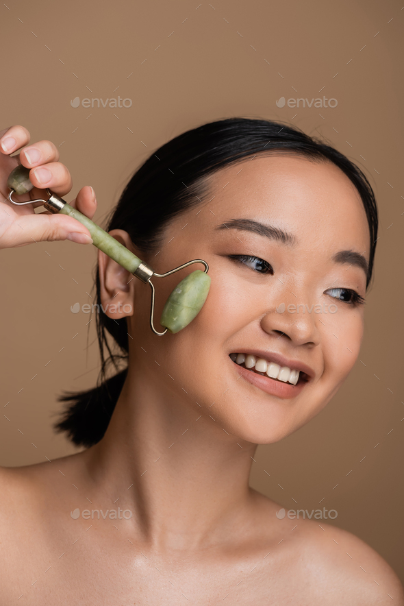 Positive Asian Model With Naked Shoulders Using Jade Roller On Face