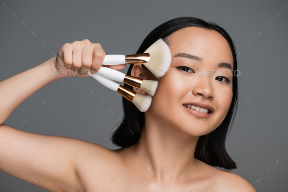 Happy Asian Woman With Bare Shoulders And Natural Makeup Holding