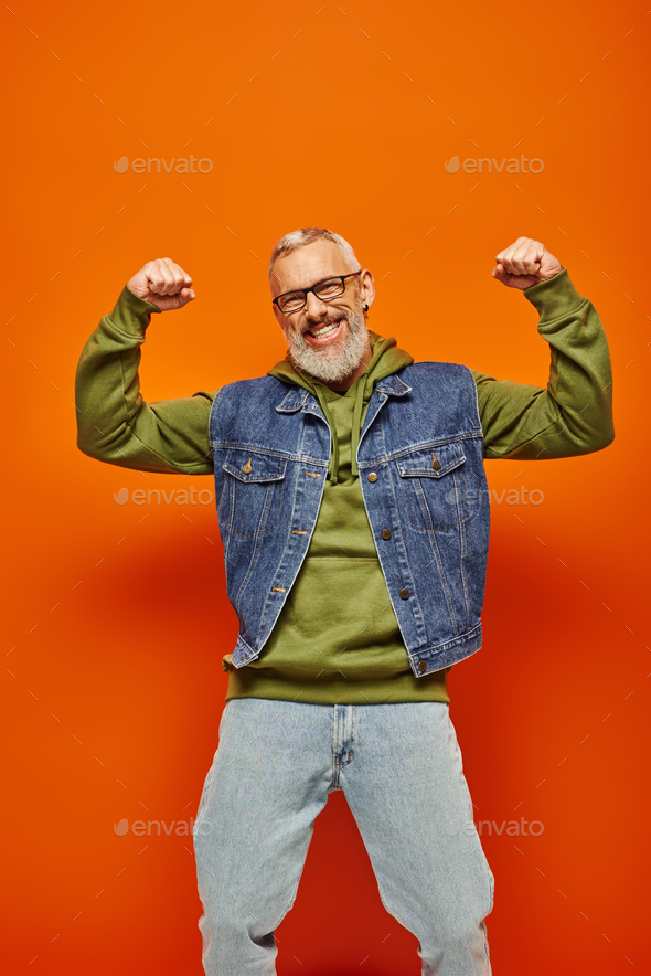 Cheerful Good Looking Mature Man In Denim Vest Posing With Arms Raised