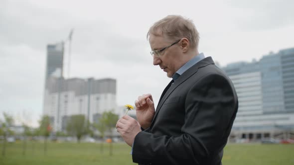 Disappointed Man in Suit Tearing Off Dandelion Flower Petals Outside Office, Upset Manager alt