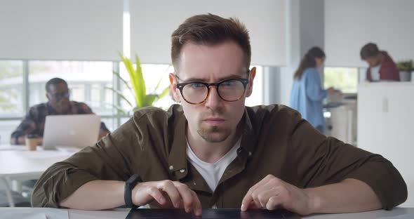 Concentrated Man Wearing Eyeglasses and Casual Shirt Using Laptop for Work Sitting in Modern Office alt